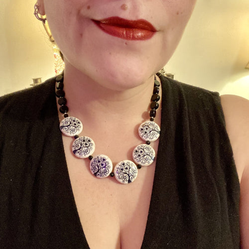This eye-catching, sizable and conspicuous black stone beads create a powerful accent piece. Crafted of reconstituted quartzite lentil beads in a tree pattern, these beads measure approximately 24mm. To enhance their effect, a round necklace of black glass beads is included. Perfect for casual or formal wear, this necklace adds an elegant finish to any ensemble. Matching earrings feature white rose reconstituted quartzite beads, completing the set.  Measurements: Necklace is 18 