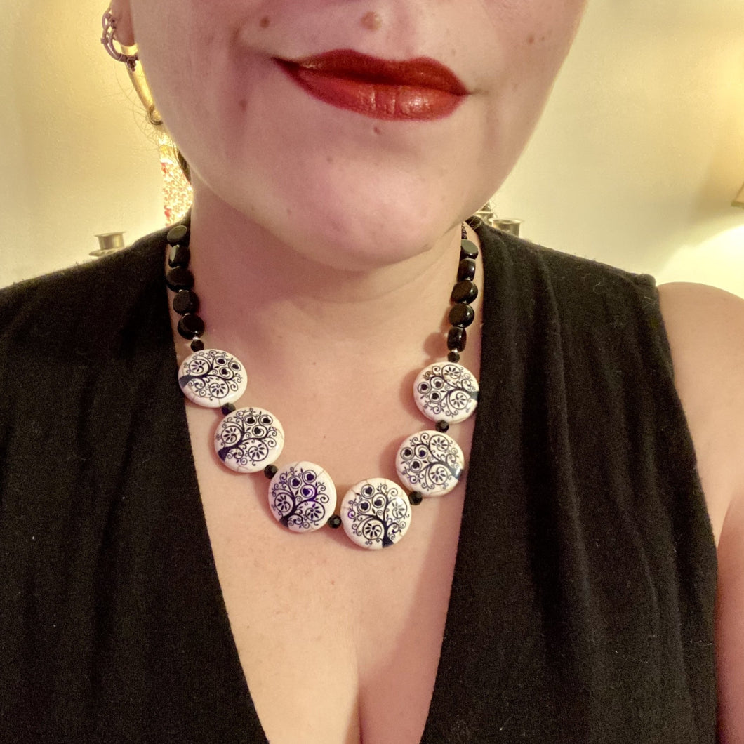 This eye-catching, sizable and conspicuous black stone beads create a powerful accent piece. Crafted of reconstituted quartzite lentil beads in a tree pattern, these beads measure approximately 24mm. To enhance their effect, a round necklace of black glass beads is included. Perfect for casual or formal wear, this necklace adds an elegant finish to any ensemble. Matching earrings feature white rose reconstituted quartzite beads, completing the set.  Measurements: Necklace is 18 