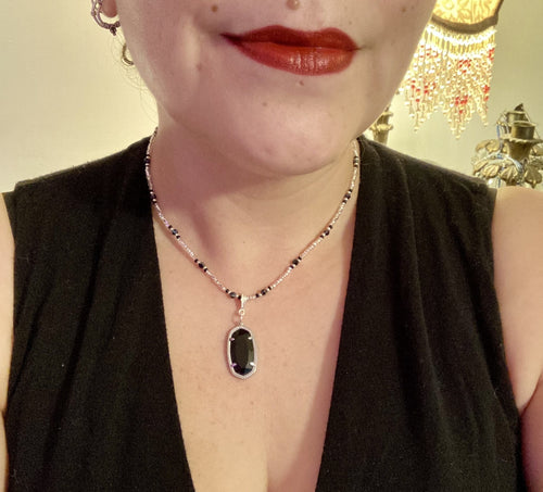 This dainty necklace is full of black and silver shimmery glass beads. A length black oval shaped glass bead hangs low to add length to this necklace.  It's the perfect necklace to add a little elegance to any outfit. Will go with any outfit, dress it up or down, this necklace will complete any look. This beauty is a must-have, add it to your jewelry collection.  Measurements: Necklace is 15 1/2” adjustable up to 18
