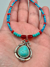 Load image into Gallery viewer, This captivating Southwestern style necklace features a two-strand design of bold and vibrant turquoise and red glass beads. At the center, a bright turquoise pendant is framed in a distinctive design. Measurements:  Necklace is 16 1/2 ” adjustable up to 18"
