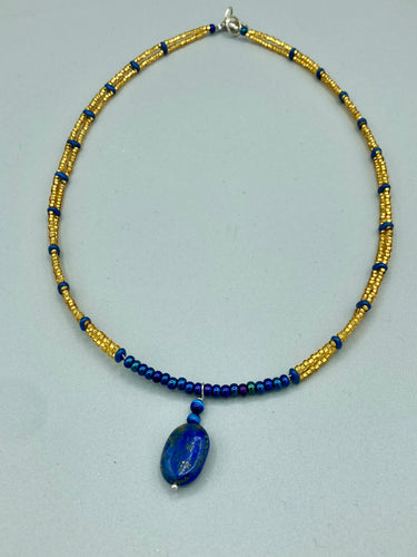 This Lapis pendant necklace features dark blue cats eye beads and two strands of gold glass beads with dark blue double hole beads. The large multi-colored glass beads provide remarkable shimmer and a full range of colors, such as purples, blues, greens, and golds, that enhances the lapis stone pendant.   Measurements:   Necklace is 19” in length 