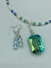 Load image into Gallery viewer, These earrings feature two shimmery iridescent glass beads with a single silver glass bead.  Measurements: 1 1/2” in length
