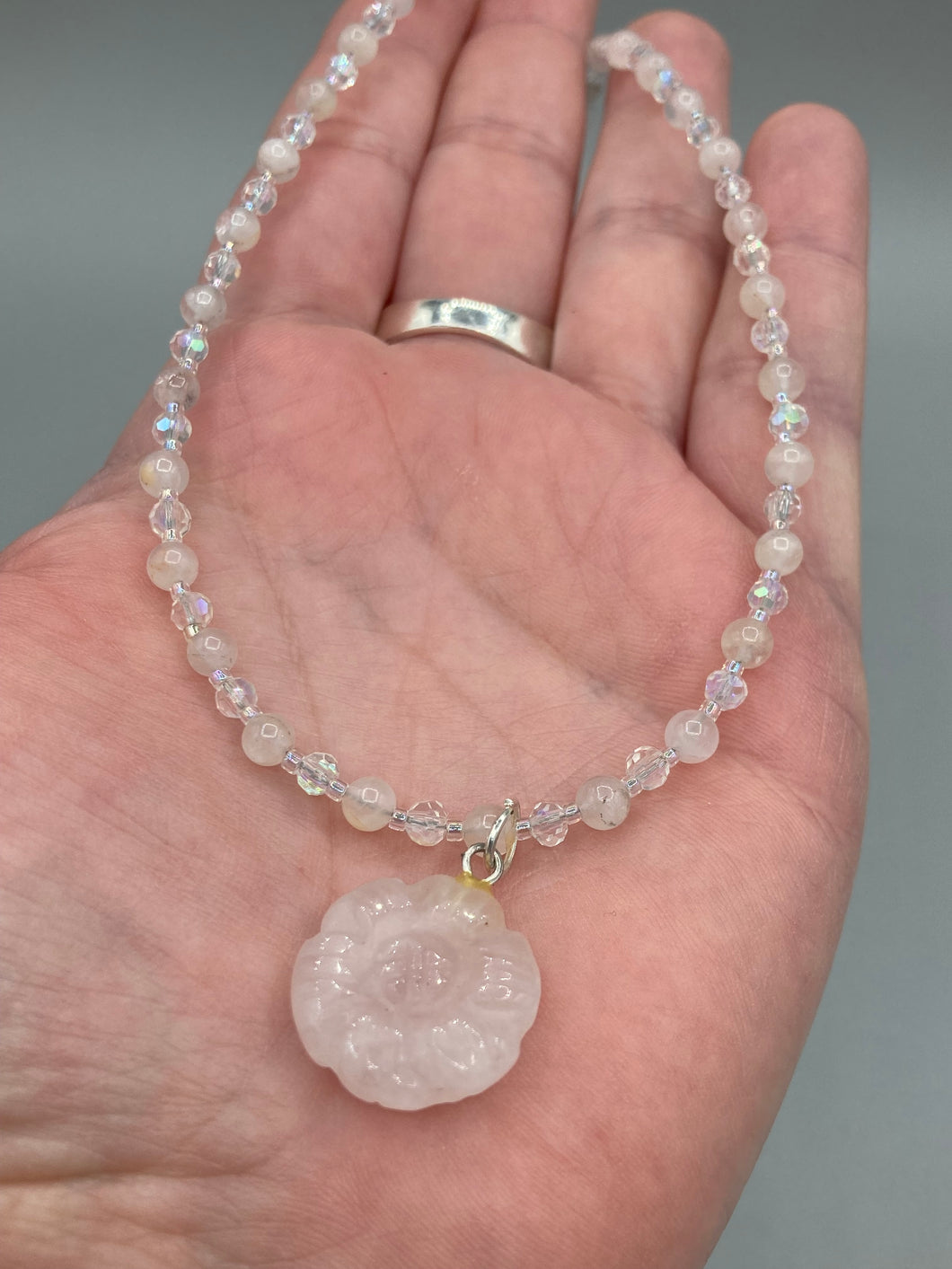 This elegant necklace is adorned with a beautiful rose quartz pendant featuring an intricate floral cutout, complemented by small round rose quartz beads with an iridescent glass finish.  Measurements:  Necklace is 18 1/2”