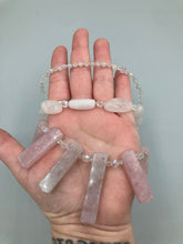 Load image into Gallery viewer, This impressive three-strand necklace is crafted from natural rose quartz stones and iridescent glass beads. The shortest strand is composed of petite round rose quartz beads, while the second strand contains an array of rectangular-shaped rose quartz and iridescent glass beads. The longest strand has long, vertical rectangular-shaped rose quartz beads, creating an elegant display across the chest.  This necklace is an impressive, dynamic accessory.  Necklace is 17: in length, can be adjusted to 19&quot;
