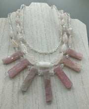 Load image into Gallery viewer, This impressive three-strand necklace is crafted from natural rose quartz stones and iridescent glass beads. The shortest strand is composed of petite round rose quartz beads, while the second strand contains an array of rectangular-shaped rose quartz and iridescent glass beads. The longest strand has long, vertical rectangular-shaped rose quartz beads, creating an elegant display across the chest.  This necklace is an impressive, dynamic accessory.  Necklace is 17: in length, can be adjusted to 19&quot;
