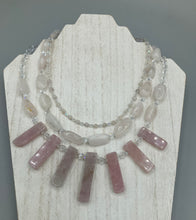 Load image into Gallery viewer, This impressive three-strand necklace is crafted from natural rose quartz stones and iridescent glass beads. The shortest strand is composed of petite round rose quartz beads, while the second strand contains an array of rectangular-shaped rose quartz and iridescent glass beads. The longest strand has long, vertical rectangular-shaped rose quartz beads, creating an elegant display across the chest.  This necklace is an impressive, dynamic accessory.  Necklace is 17: in length, can be adjusted to 19&quot;
