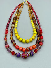Load image into Gallery viewer, This necklace consists of three strands with a multitude of shades ranging from red to orange, gold, and amber, providing a captivating visual combination. Crafted with a combination of glass, ceramic and metal beads, this eye-catching piece of jewelry radiates power and strength.  Measurements:  Necklace is 16” in length, can be adjusted up to 17 1/2&quot;

