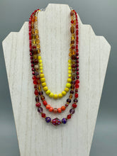 Load image into Gallery viewer, This necklace consists of three strands with a multitude of shades ranging from red to orange, gold, and amber, providing a captivating visual combination. Crafted with a combination of glass, ceramic and metal beads, this eye-catching piece of jewelry radiates power and strength.  Measurements:  Necklace is 16” in length, can be adjusted up to 17 1/2&quot;
