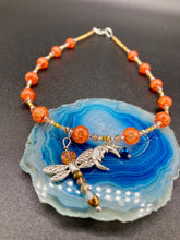 Load image into Gallery viewer, This bright orange, adjustable, choker-style necklace is adorned with beaded glass and a striking crescent moon charm and dragonfly pendant. Accessorize with matching dragonfly earrings for an eye-catching, complementary look that captures the warmth of summer. Perfect for any outfit, its vibrant colors will make a statement and complete any look.  Measurements: Necklace is 16 1/2”adjustable up to 19&quot; 
