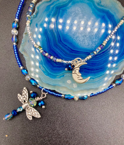 Soft Blue and Silver Adjustable Choker Style Glass Beaded Necklace With A Silver Dragonfly Pendant. Whimsical smiling crescent moon dangling charm comes matching earrings. Dainty elegant summer necklace has the perfect witchy, whimsical, magical, starry night look, it will complete any look.  Measurements: Necklace is 15” adjustable up to 18