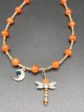Load image into Gallery viewer, This bright orange, adjustable, choker-style necklace is adorned with beaded glass and a striking crescent moon charm and dragonfly pendant. Accessorize with matching dragonfly earrings for an eye-catching, complementary look that captures the warmth of summer. Perfect for any outfit, its vibrant colors will make a statement and complete any look.  Measurements: Necklace is 16 1/2”adjustable up to 19&quot; 
