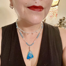 Load image into Gallery viewer, This exquisite necklace features a vibrant Sea Blue Agate Natural Stone Pendant and two strands of multi-colored glass beaded necklace. An adjustable collar-style strand contains small, light blue beads and lots of iridescent double-hole beads for shimmer and sparkle. The longer strand features larger blue glass beads interspersed with clear and silver beads for a sophisticated, draped look. It's finished with a set of dainty matching earrings for a complete look. Necklace is 14”adjustable up to 18"
