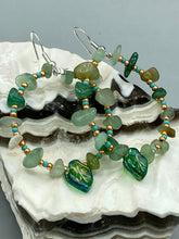 Load image into Gallery viewer, Natural aventurine stone chips, turquoise, and gold glass beads are strung together to form these stylish hoop earrings. The dark green pressed glass leaf charm complements the design, creating an iridescent, shimmery finish with subtle hues of gold, purple, blue, and pink. Measurements: 2&quot; length
