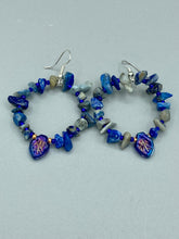 Load image into Gallery viewer, These Lapis Stone Chip Beaded Hoop Earrings feature a dark blue-tone pressed glass leaf charm with an iridescent shimmer finish showcasing hues of gold, purple, blue and pink. The earrings display natural lapis stone chips and royal blue with gold glass beads.  Measurements: 1 1/2&quot; length

