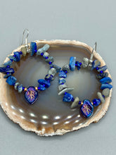 Load image into Gallery viewer, These Lapis Stone Chip Beaded Hoop Earrings feature a dark blue-tone pressed glass leaf charm with an iridescent shimmer finish showcasing hues of gold, purple, blue and pink. The earrings display natural lapis stone chips and royal blue with gold glass beads.  Measurements: 1 1/2&quot; length
