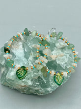 Load image into Gallery viewer, These handmade hoop earrings feature natural Aventurine and White Moon Stone chips along with turquoise and gold glass beads. The light green-toned pressed glass leaf charm beautifully shimmers with iridescent hues of gold, purple, blue, and pink. Measurements: 2&quot; length
