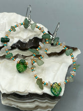 Load image into Gallery viewer, These handmade hoop earrings feature natural Aventurine and White Moon Stone chips along with turquoise and gold glass beads. The light green-toned pressed glass leaf charm beautifully shimmers with iridescent hues of gold, purple, blue, and pink. Measurements: 2&quot; length
