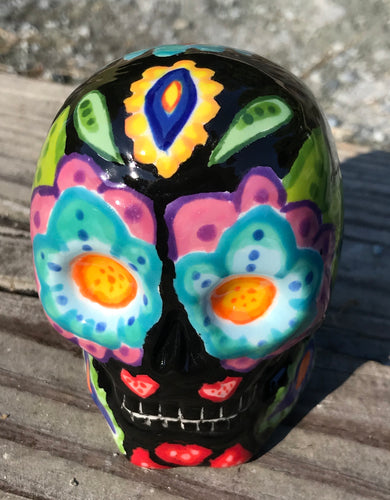This black ceramic sugar skull, inspired by nature, is adorned with hand-painted floral motifs, hearts, leaves and colorful accents. Its vibrant style and intricate details create a stunning Dia De Los Muertos calavera. Perfect for creating ofrendas to celebrate the Day of the Dead. Measurements: H 2 3/4” x W 2” x D 2”