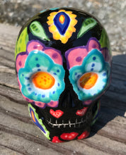 Load image into Gallery viewer, This black ceramic sugar skull, inspired by nature, is adorned with hand-painted floral motifs, hearts, leaves and colorful accents. Its vibrant style and intricate details create a stunning Dia De Los Muertos calavera. Perfect for creating ofrendas to celebrate the Day of the Dead. Measurements: H 2 3/4” x W 2” x D 2”
