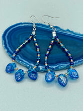 Load image into Gallery viewer, These striking Royal Blue Pressed Glass Leaf Beaded Hoop Earrings feature a shimmery finish with a hint of gold, purple, blue and pink. Gold, dark and light blue glass beads complete the piece.  Measurements: 2 1/2&quot; length
