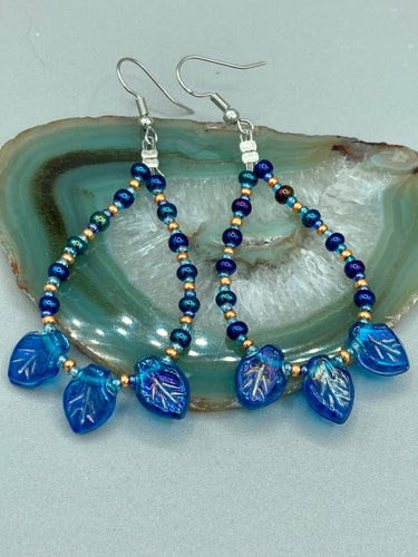 These striking Royal Blue Pressed Glass Leaf Beaded Hoop Earrings feature a shimmery finish with a hint of gold, purple, blue and pink. Gold, dark and light blue glass beads complete the piece.  Measurements: 2 1/2