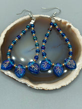 Load image into Gallery viewer, These striking Royal Blue Pressed Glass Leaf Beaded Hoop Earrings feature a shimmery finish with a hint of gold, purple, blue and pink. Gold, dark and light blue glass beads complete the piece.  Measurements: 2 1/2&quot; length
