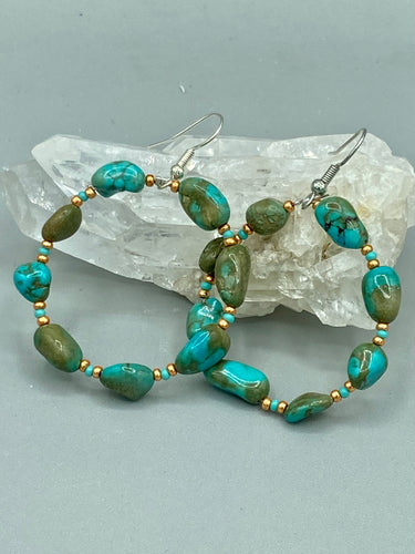 Our Blue-Green Magnesite Stone Beaded Hoop Earrings provide a nature-inspired look that is perfect for any boho-chic style. These earrings feature natural magnesite stone beads with small beads of turquoise and gold glass for subtle accent. Show off your bohemian look with these eye-catching hoops. Measurements: 2