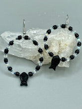Load image into Gallery viewer, This sophisticated pair of earrings features a black glass fish bead, complemented by small iridescent and dark gray color glass beads, with eye and fin details. Measurements: 2” in length  
