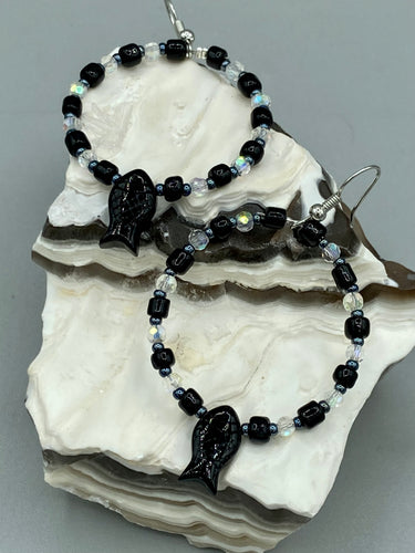 This sophisticated pair of earrings features a black glass fish bead, complemented by small iridescent and dark gray color glass beads, with eye and fin details. Measurements: 2” in length  