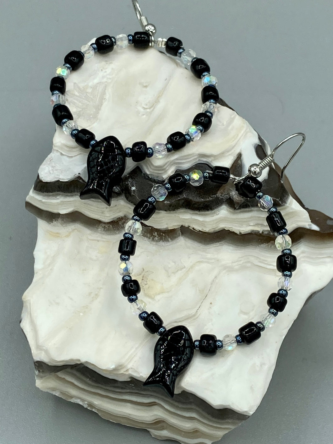 This sophisticated pair of earrings features a black glass fish bead, complemented by small iridescent and dark gray color glass beads, with eye and fin details. Measurements: 2” in length  