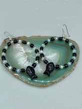 Load image into Gallery viewer, This sophisticated pair of earrings features a black glass fish bead, complemented by small iridescent and dark gray color glass beads, with eye and fin details. Measurements: 2” in length  

