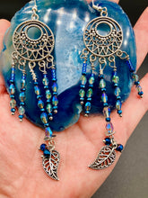 Load image into Gallery viewer, These intricate moroccan blue Inspired large chandelier earrings boast five strands of blue and iridescent glass beads of various hues, including silver and gold. Additionally, two small dark blue glass beads with a silver leaf add a touch of dimension and motion. The perfect addition to any Fairy Princess or whimsical aesthetic.  Measurements: 4” in length

