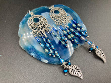 Load image into Gallery viewer, These intricate moroccan blue Inspired large chandelier earrings boast five strands of blue and iridescent glass beads of various hues, including silver and gold. Additionally, two small dark blue glass beads with a silver leaf add a touch of dimension and motion. The perfect addition to any Fairy Princess or whimsical aesthetic.  Measurements: 4” in length
