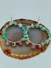 Load image into Gallery viewer, These Aventurine Stone Chip Beaded Hoop Earrings feature natural aventurine stone chips, turquoise, and gold glass beads. The amber-tone pressed glass leaf charm has an iridescent shimmer finish, with subtle accents of gold, purple, blue, and pink. Measurements: 2&quot; length
