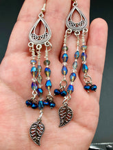 Load image into Gallery viewer, Blue Moroccan Inspired Large Chandelier Earrings. Three strands of beautiful blue and iridescent glass beads with intricate silver plated leaf charms create a lot of movement. Versatile, perfect for whimsical fairy princes, good witch, hippie nature lovers looks. These earring will compliment any look.  Measurements: 3 1/2” in length
