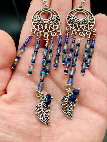These intricate moroccan blue Inspired large chandelier earrings boast five strands of blue and iridescent glass beads of various hues, including silver and gold. Additionally, two small dark blue glass beads with a silver leaf add a touch of dimension and motion. The perfect addition to any Fairy Princess or whimsical aesthetic.  Measurements: 4” in length