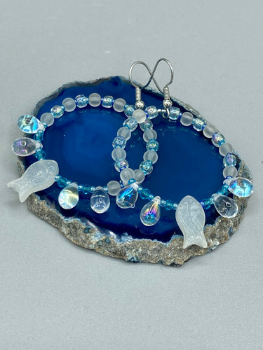 This stylish set of earrings feature milky white fish-shaped glass beads, complemented by light blue and iridescent teardrop glass beads. The fish-shaped glass beads feature intricate details, including fins and an eye.  Measurements: 1 7/8” in length 