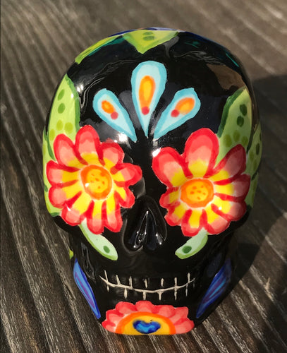 Inspired by nature, this ceramic skull statuette is full of vibrant color and intricate details. The primary color is black with multi-color floral motifs that are painted across the skull, along with hearts and leaves and lively colorful accents around the entire skull. 