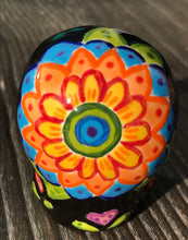 Load image into Gallery viewer, Inspired by nature, this ceramic skull statuette is full of vibrant color and intricate details. The primary color is black with multi-color floral motifs that are painted across the skull, along with hearts and leaves and lively colorful accents around the entire skull. 
