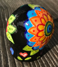 Load image into Gallery viewer, Inspired by nature, this ceramic skull statuette is full of vibrant color and intricate details. The primary color is black with multi-color floral motifs that are painted across the skull, along with hearts and leaves and lively colorful accents around the entire skull. 

