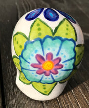 Load image into Gallery viewer, Inspired by nature, this ceramic skull statuette is full of vibrant color and intricate details that I hand painted. The primary color is white with multi-color floral motifs that are painted across the skull, along with hearts and leaves and lively colorful accents around the entire skull. 
