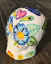 Load image into Gallery viewer, Inspired by nature, this ceramic skull statuette is full of vibrant color and intricate details that I hand painted. The primary color is white with multi-color floral motifs that are painted across the skull, along with hearts and leaves and lively colorful accents around the entire skull. 

