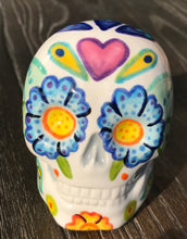 Load image into Gallery viewer, Inspired by nature, this ceramic skull statuette is full of vibrant color and intricate details that I hand painted. The primary color is white with multi-color floral motifs that are painted across the skull, along with hearts and leaves and lively colorful accents around the entire skull. 
