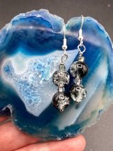 Load image into Gallery viewer, Two large round glass beads with shimmer of black, silver and gray  tones, fish hook style earrings 1 1/4”
