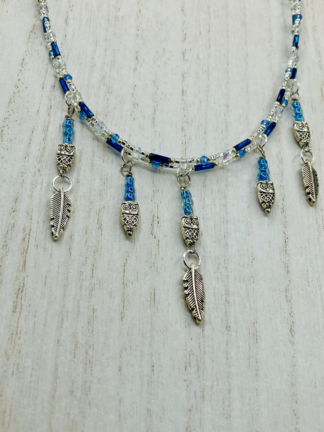 Silver And Blue Wise Owl Charm Choker Style Glass Beaded Necklace. Whimsical and elegant necklace has two different styles of tiny cute owls with silver plated feathers. Some say wearing an owl pendant around your neck is just want you need for a better connection to your intuition. Owls symbolize wisdom, the wisdom that comes to prevent hasting rushing or being impulsive. Necklace comes with matching earrings, necklace is 16” adjustable up to 18