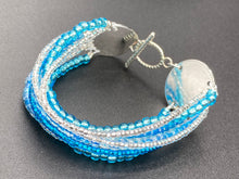 Load image into Gallery viewer, This bracelet is a chic, minimalistic design with nine beaded strands that feature various blue and silver glass beads. It measures 7 1/2&quot; in length and has been crafted with inspiration from the ocean blue waves.
