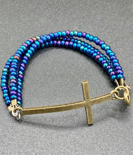 Load image into Gallery viewer, For Positivity and Faith, Shimmery Blue Glass Beaded Bracelet With Curved Horizontal Brass Cross. This bracelet has a large brass cross that is slightly curved to be comfortably worm around your wrist. I created three glass beaded strands that have a wide variety of blue, purple, green, and gold tones. Measurements: 7 1/2&quot; in length, brass cross measures 2&quot; in length
