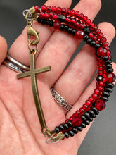 Load image into Gallery viewer, For Positivity and Faith, Shimmery Red And Black Glass Beaded Bracelet With Curved Horizontal Brass Cross. This bracelet has a large brass cross that is slightly curved to be comfortably worm around your wrist.  I created four different black and red glass beads strands. Measurements: 7 1/2&quot; in length, brass cross measures 2&quot; in length. 
