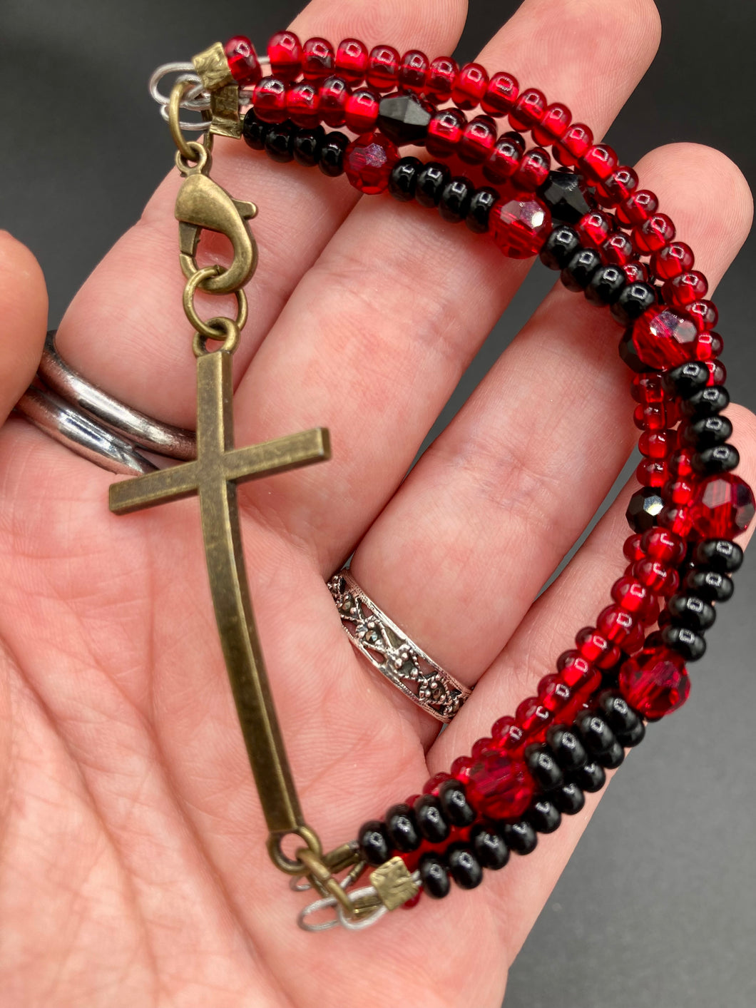 For Positivity and Faith, Shimmery Red And Black Glass Beaded Bracelet With Curved Horizontal Brass Cross. This bracelet has a large brass cross that is slightly curved to be comfortably worm around your wrist.  I created four different black and red glass beads strands. Measurements: 7 1/2