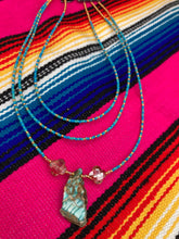 Load image into Gallery viewer, This vibrant and enchanting Southwestern Style inspired necklace is comprised of three strands. The first two feature a mix of blue and green turquoise and gold glass beads, while the longest strand features a howlite stone chip dyed turquoise and shimmery cross faceted champaign color glass beads for a dramatic look.  Measurements: The Necklace is 16” and can be adjusted up to 18" 
